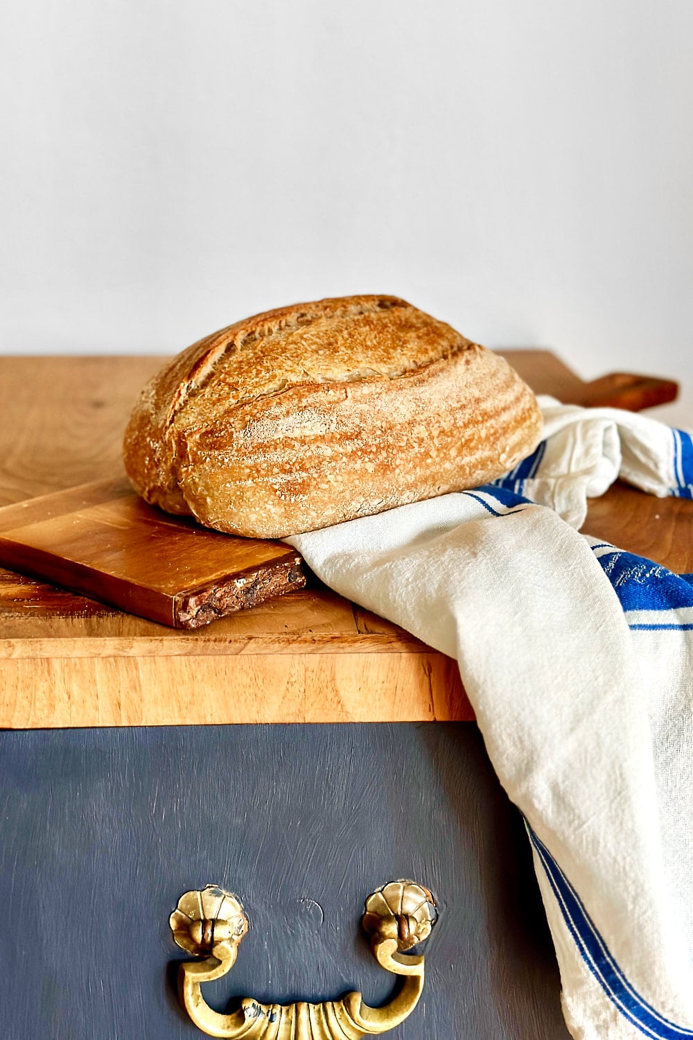 A crispy loaf of rosemary sourdough bread on a wooden board with a white linen towel next to it.