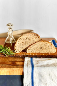 Freshly baked rosemary sourdough bread with a small jug of olive oil and fresh twigs of rosemary next to it.