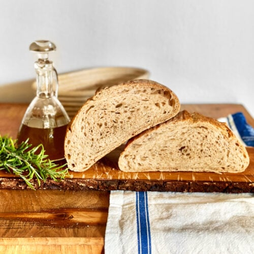 Freshly baked rosemary sourdough bread with a small jug of olive oil and fresh twigs of rosemary next to it.