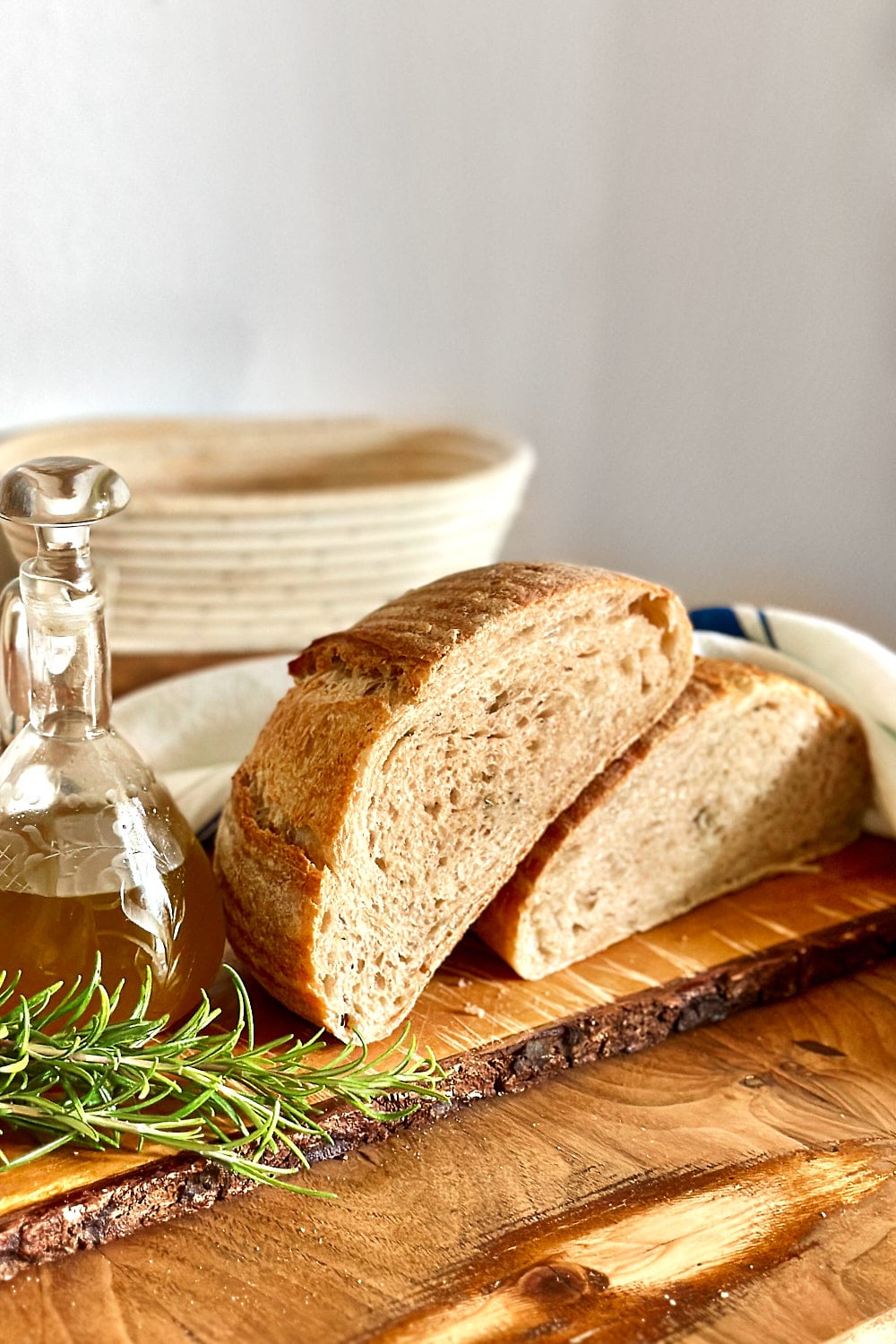A loaf of rosemary sourdough bread with a small jug of olive oil and fresh twigs of rosemary next to it.