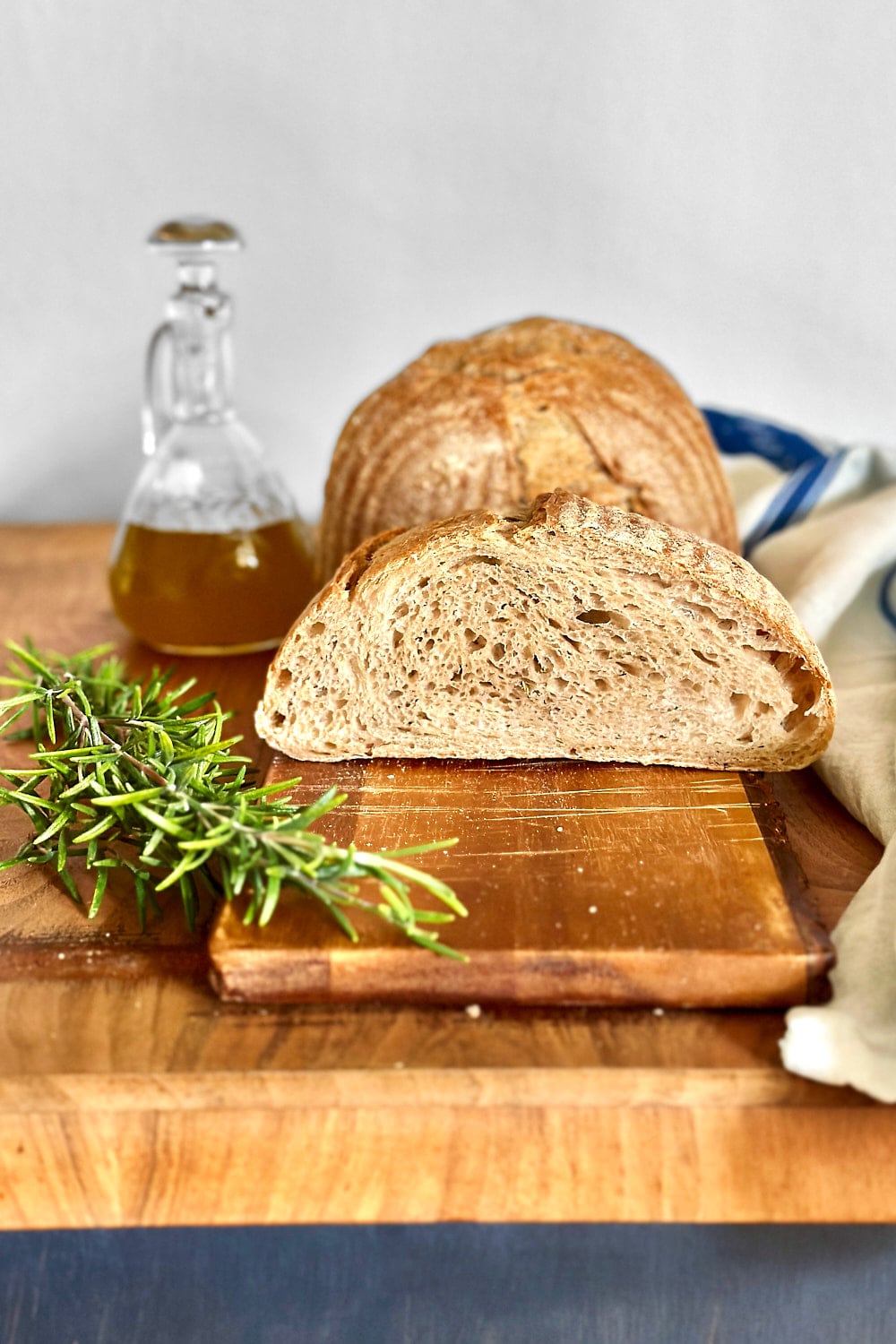 A loaf of rosemary sourdough bread cut in half on a wooden board.