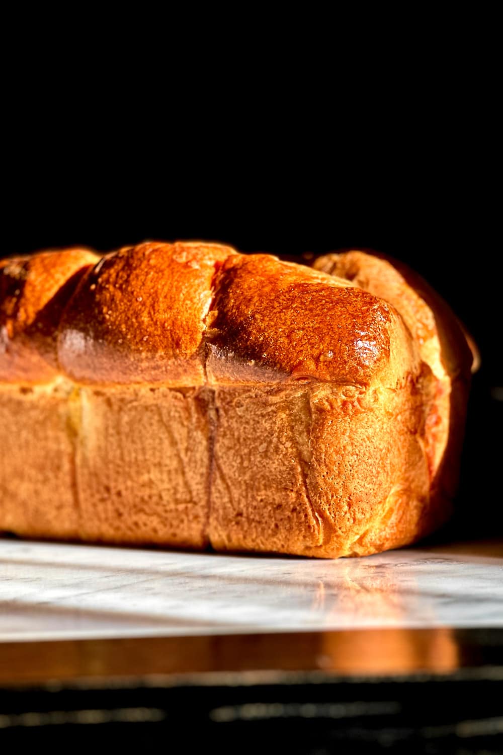A freshly baked sourdough brioche on a white marble surface in golden hour sunlight.