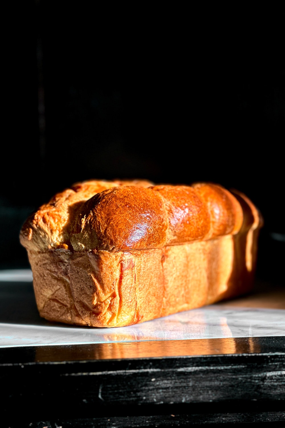 A freshly baked sourdough brioche on a white marble surface in golden hour sunlight.