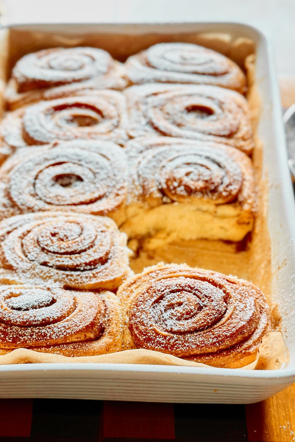 Close-up of a baking dish with freshly baked sourdough cinnamon rolls, dusted with powdered sugar.