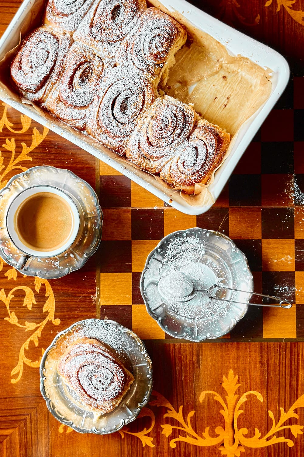 Flatlay of a baking dish with freshly baked sourdough cinnamon buns on a wooden table.