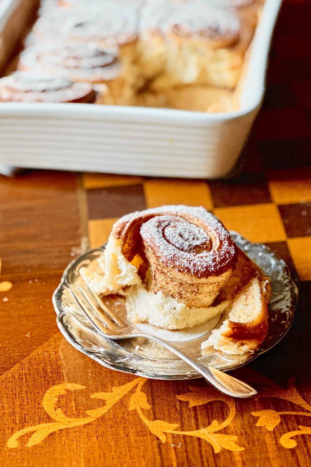 A fluffy sourdough cinnamon roll on a small plate with a silver fork.