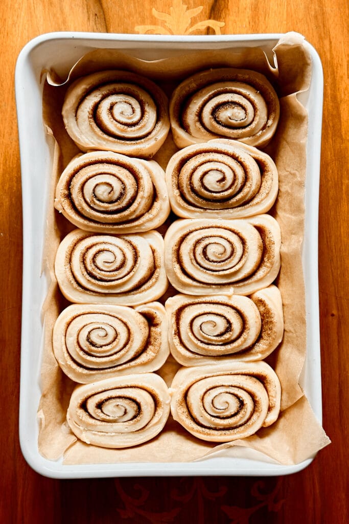 Homemade sourdough cinnamon rolls fully proofed and puffy in a white ceramic baking dish.
