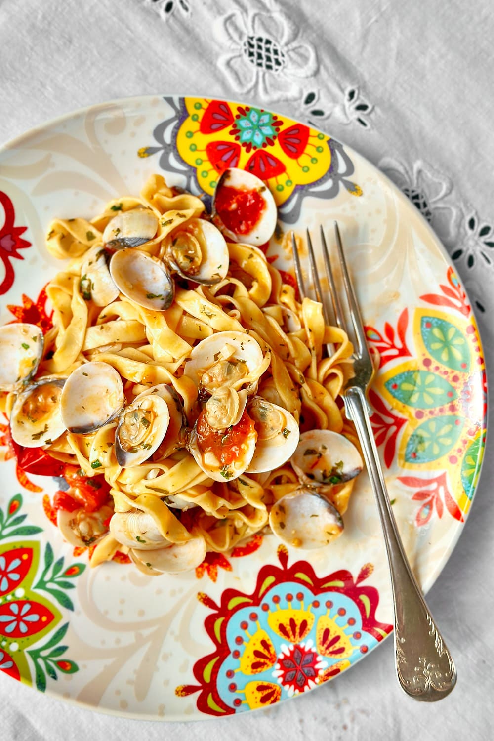 flatlay of tagliatelle alle vongole on a plate with a mediterranean pattern and a silver fork next to it.