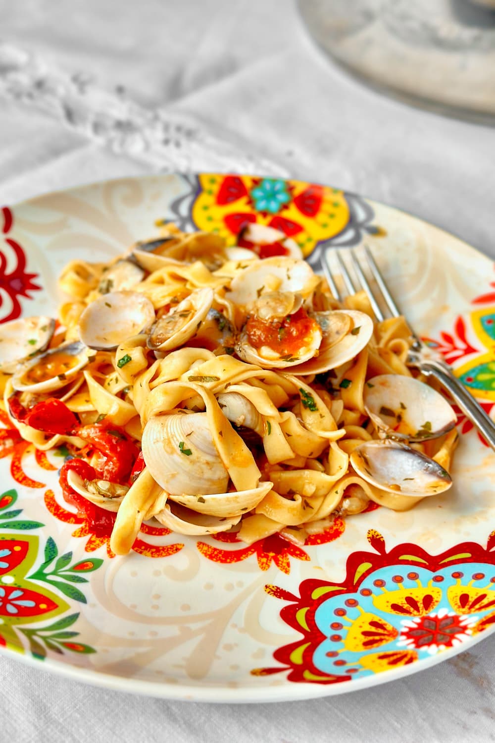 homemade tagliatelle pasta with clams on a plate with a mediterranean pattern.