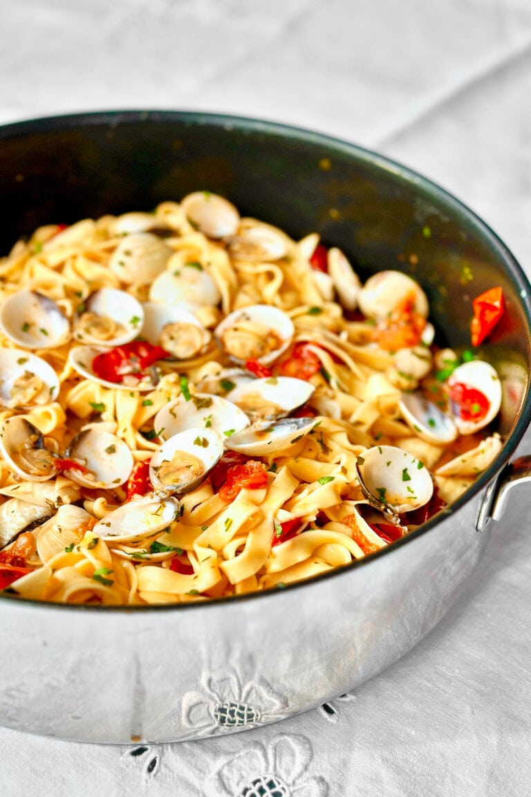 A skillet with clam pasta with cherry tomatoes in a white wine garlic sauce.