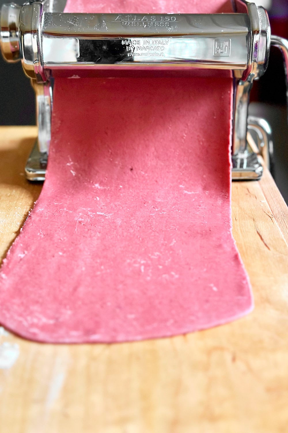 Using a pasta machine to roll the beet pasta dough out into thin pasta sheets.