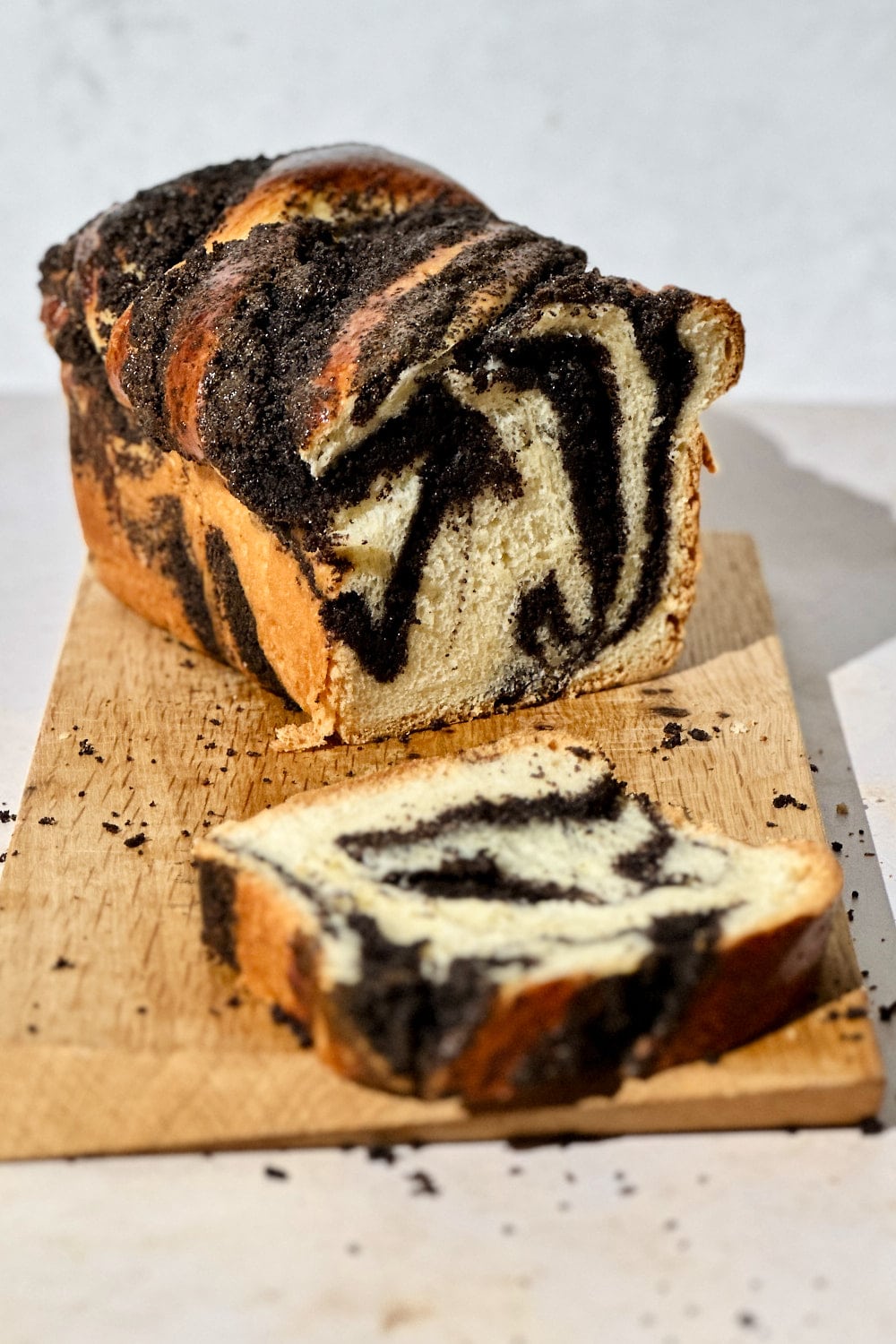 Homemade poppy seed sourdough babka on a wooden board with a slice cut off.